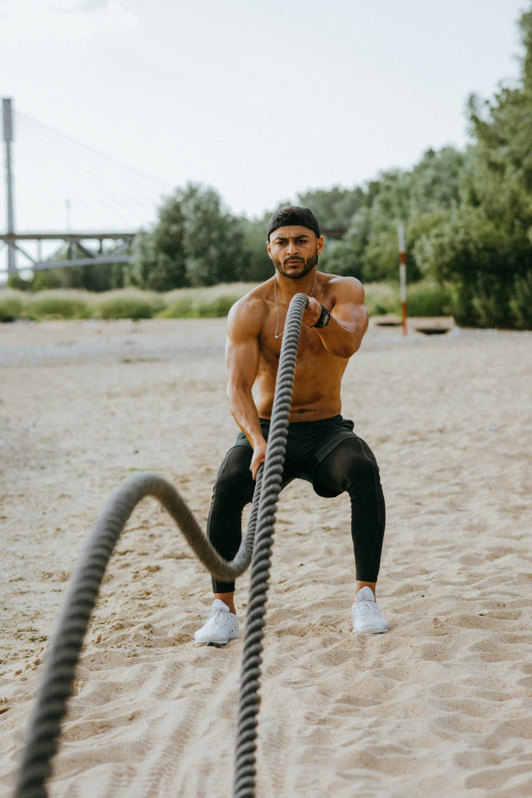 Athlete driving battle ropes on the sand — raw effort, focused sweat